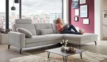 Großes graues Ecksofa im modernen Wohnzimmer mit RAL Gütezeichen Möbelqualität. Die Frau liest entspannt auf dem Sofa, das mit Kissen und Couchtisch mit Deko ausgestattet ist.